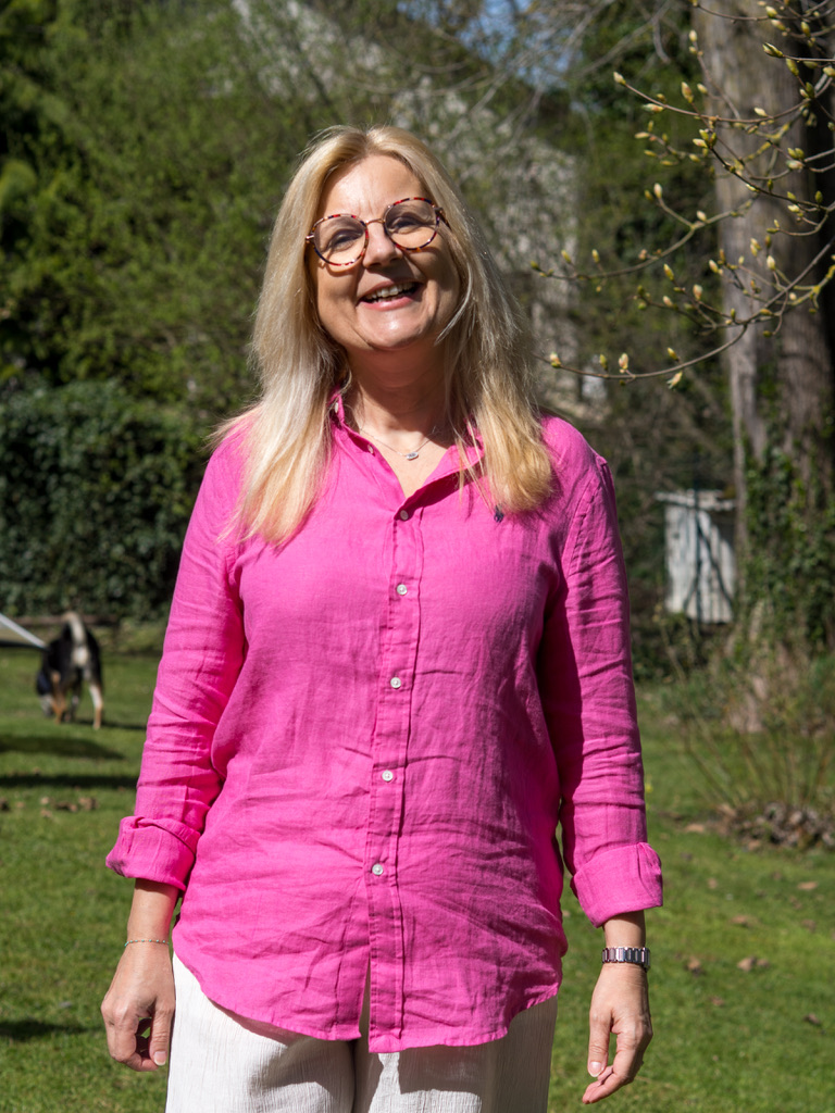 Carole Desmoulière, coach femme et couple, en chemise rose dans un jardin