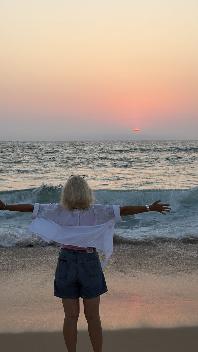 Femme face à la mer au coucher du soleil, les bras ouverts