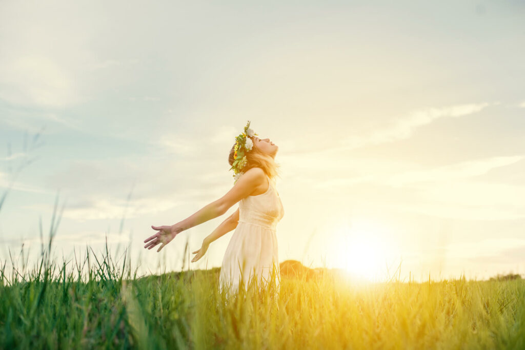 Femme les bras ouverts face au soleil dans un champ