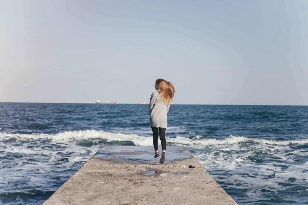 Femme seule au bout d'une jetée face à la mer